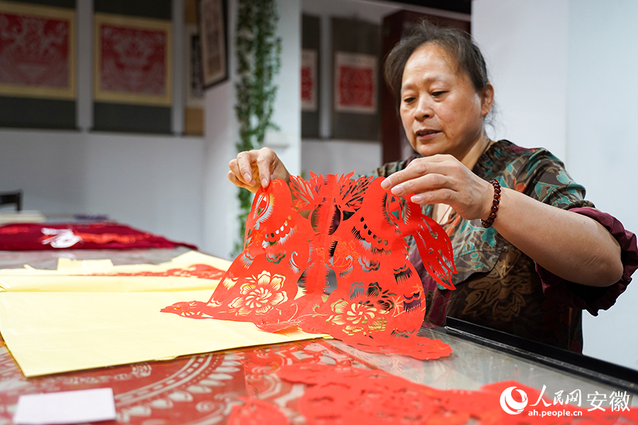 張學(xué)華正在查看修整剪紙作品。人民網(wǎng)記者 王銳攝