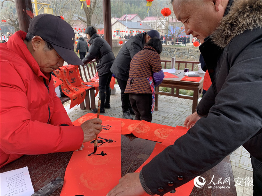 戴金才（左一）現(xiàn)場寫春聯(lián)。人民網(wǎng)記者 汪瑞華攝